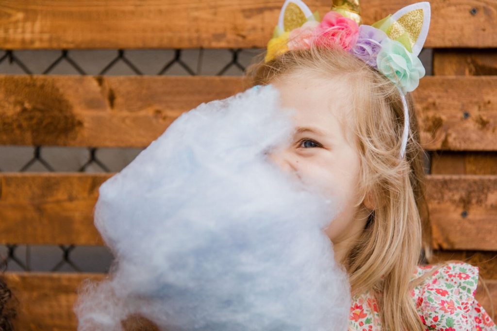 maquinas de peluches para fiestas infantiles a domicilio — Little girl wearing unicorn ears enjoying cotton candy outdoors.