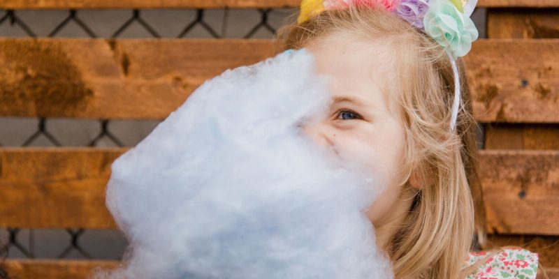 maquinas de peluches para fiestas infantiles a domicilio — Little girl wearing unicorn ears enjoying cotton candy outdoors.